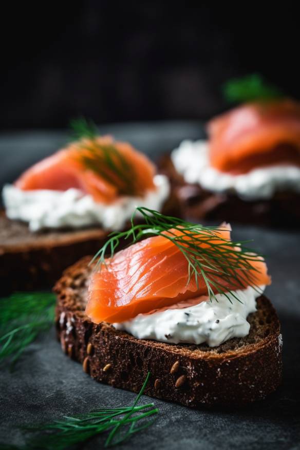 Pumpernickel-Fingerfood mit Frischkäse und Räucherlachs auf einem Teller angerichtet.