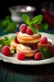 Mini-Cheesecake-Törtchen auf einem weißen Teller mit Himbeeren und Minze als Dekoration.