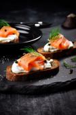 Pumpernickel-Fingerfood mit Frischkäse und Räucherlachs auf einem Teller angerichtet.