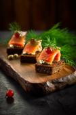 Pumpernickel-Lachs-Fingerfood auf einem Holzbrett angerichtet.