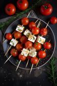 Tomaten-Feta-Spiesse auf einem Teller angerichtet.